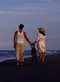 couple walking alone on a beach with a bicycle between them